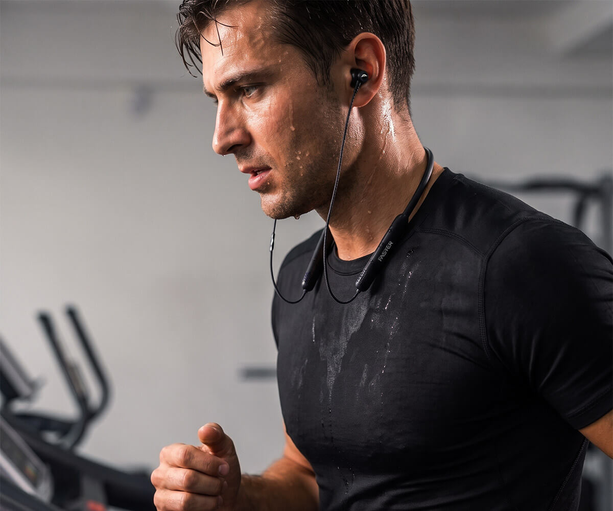 A man in a black athletic t-shirt running in a gym while wearing a black neckband.