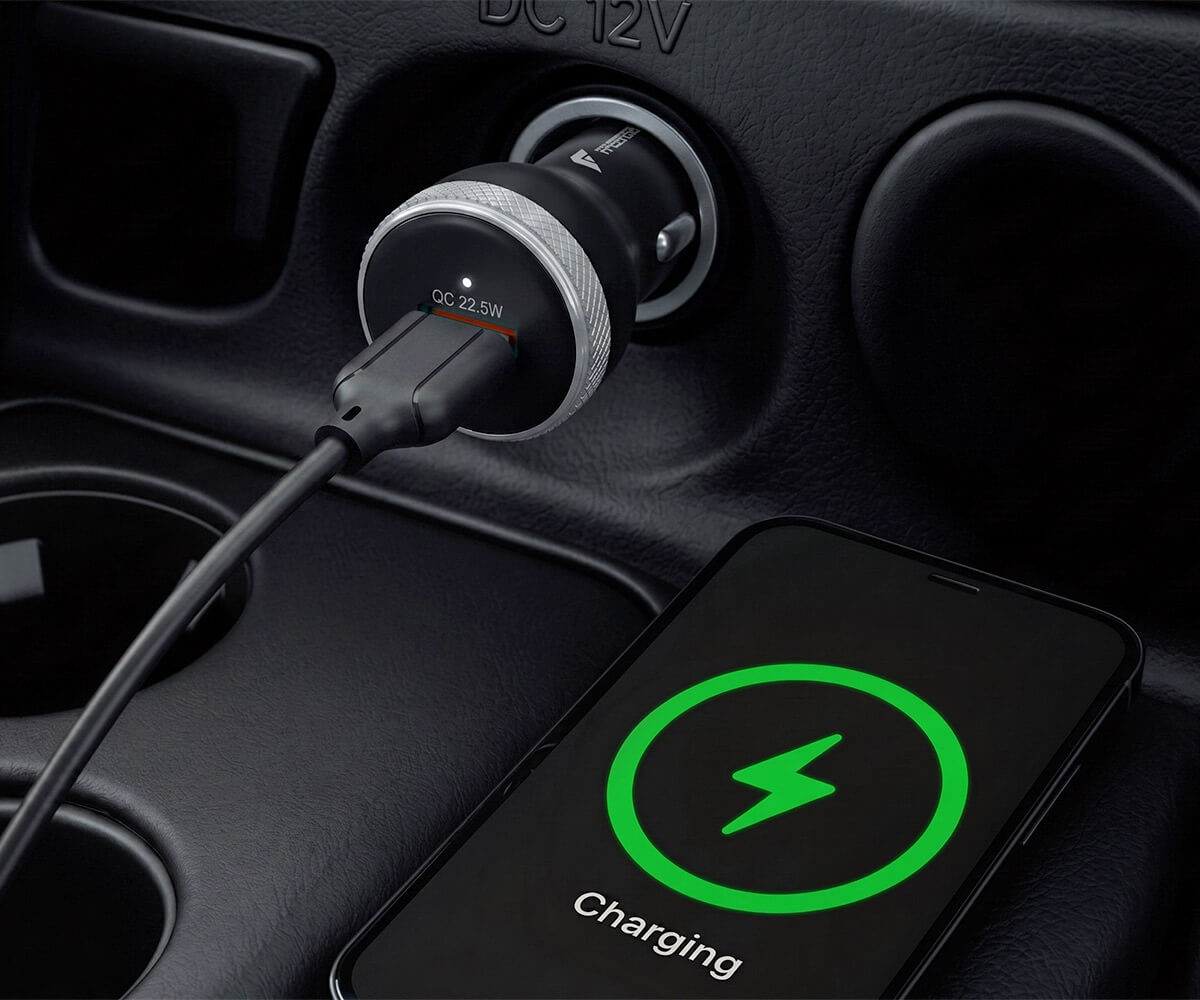 A black car charger plugged into a car port, with a smartphone lying nearby showing a green charging icon on its screen.