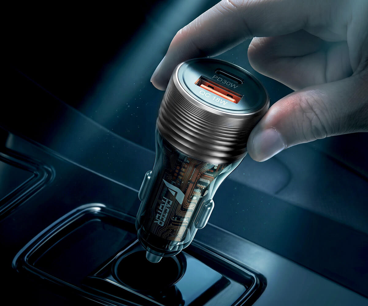 A hand inserts a metallic car charger into a cigarette lighter socket inside a car. The charger has a brushed bronze finish, a clear body showing internal circuitry, and a silver USB-C port with an orange accent.