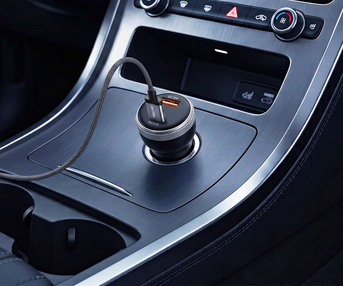 A black and silver 2-in-1 USB car charger plugged into a car's center console port, with a black cable extending to the left.