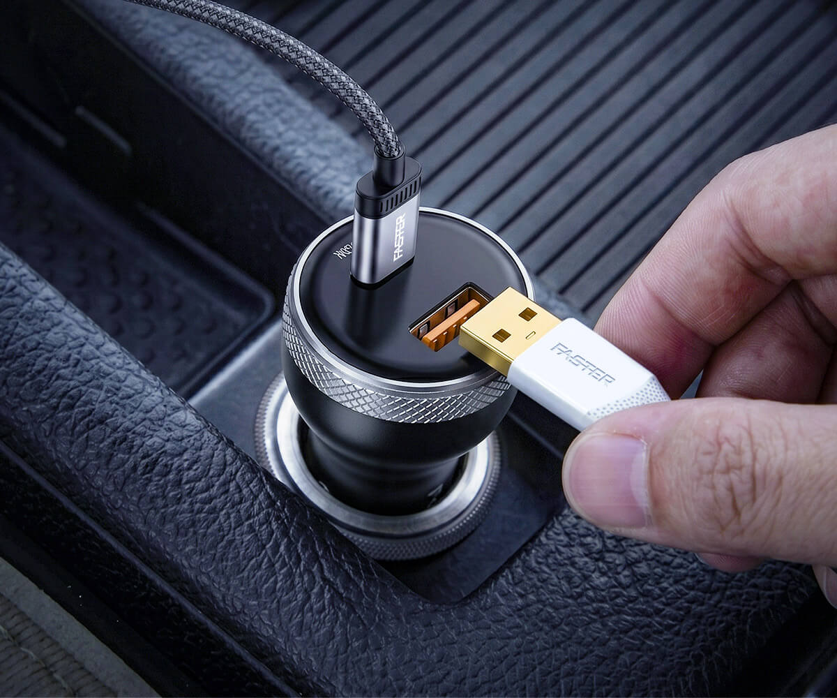 A close-up of a hand plugging a white and gold USB-C cable into a black and silver car charger, which is inserted into a black textured car dashboard.