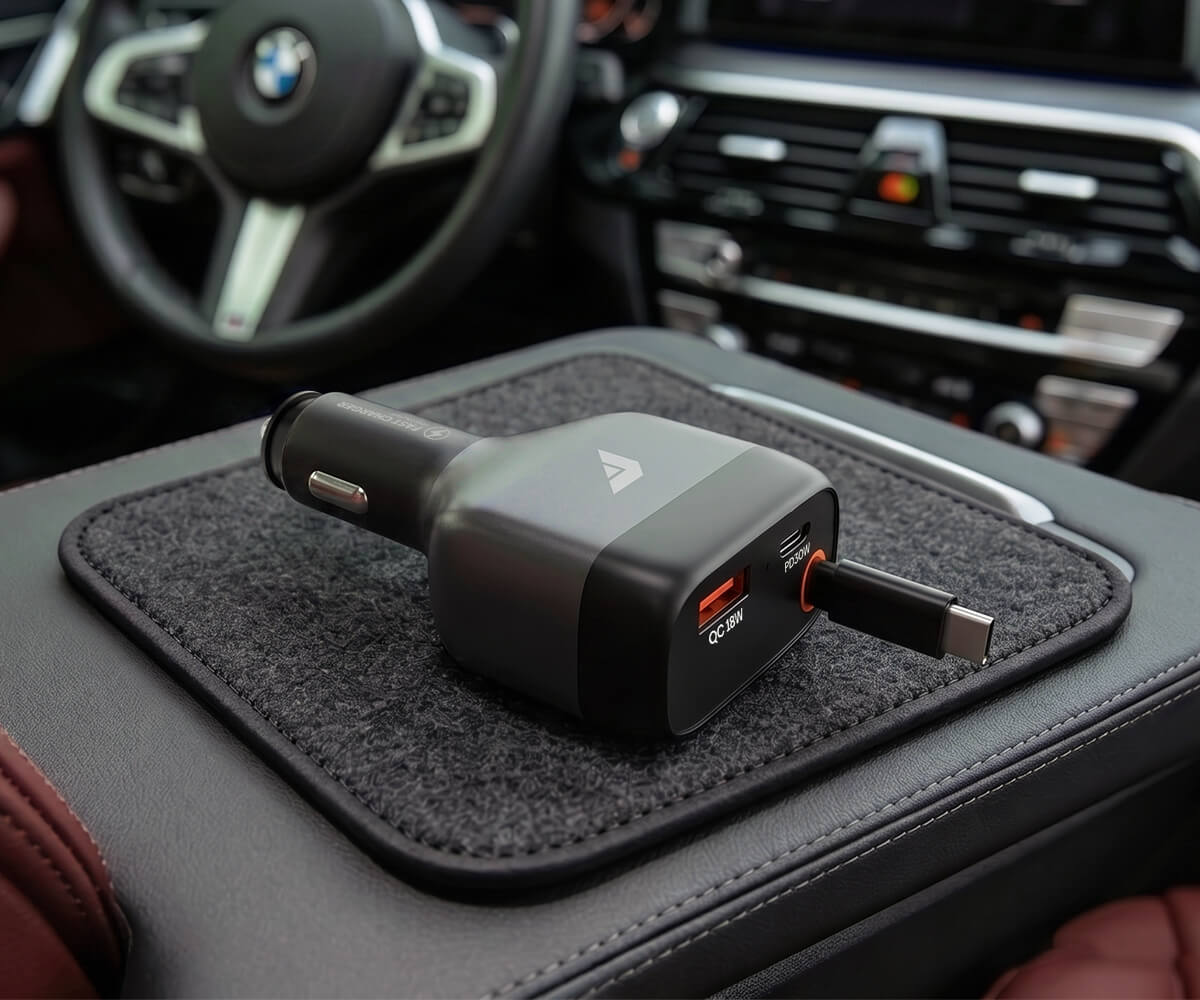 A black car cigarette lighter dual charger with USB-C and USB-A ports sits on a dark gray textured mat inside a car's center console.