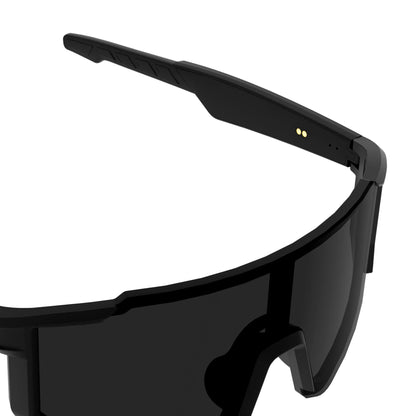 Close-up of a black wraparound shield-style smart glasses frame with dark lenses and small gold circular details on the inner temple, shown on a white background.