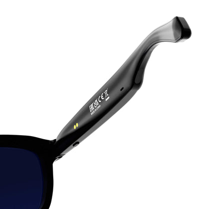 Close-up of a black sunglasses arm with dark blue lenses, showing white printed text and small yellow dots on a clean white background.