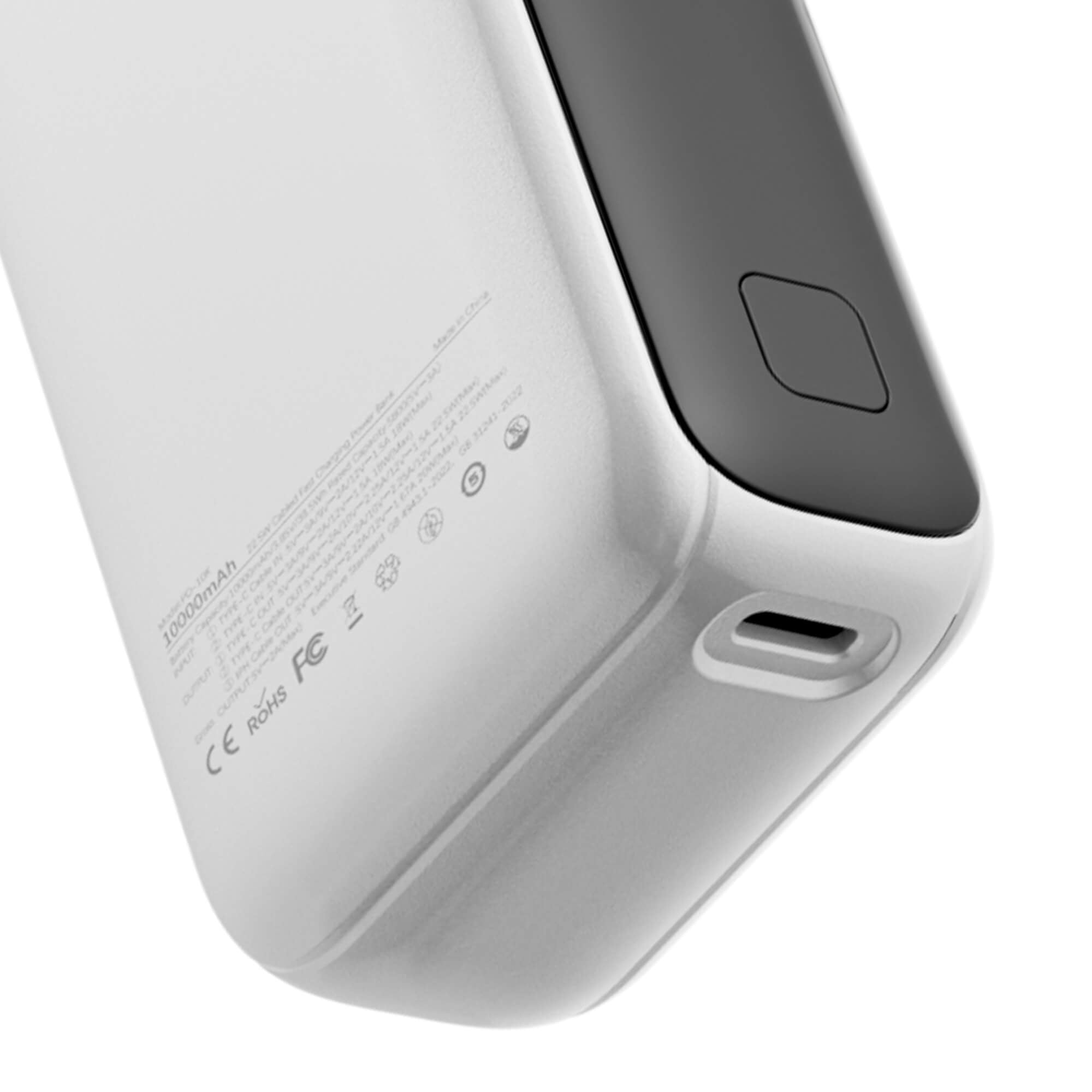 Close-up of the corner of a silver and dark gray portable power bank, showing a USB-C port and a square button, with regulatory text printed on the back.